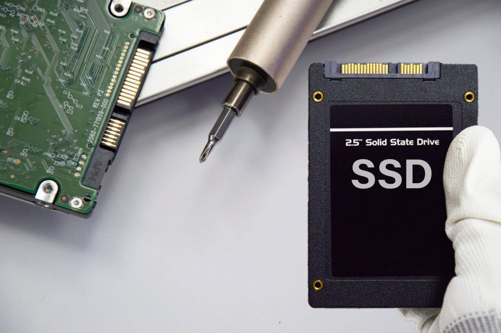 SSD disk u ruci sa zaštitnom rukavicom, pored starog hard diska i odvijača na radnoj površini